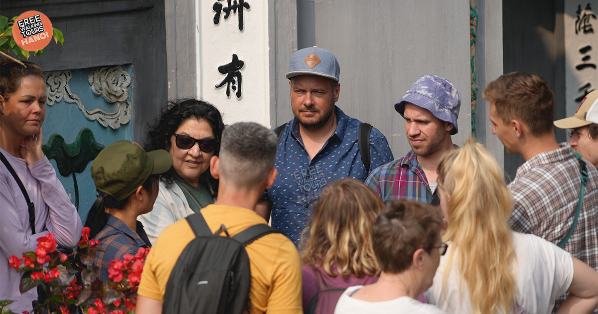 A diverse group of travelers on a free walking tour in Hanoi, led by a young Vietnamese guide